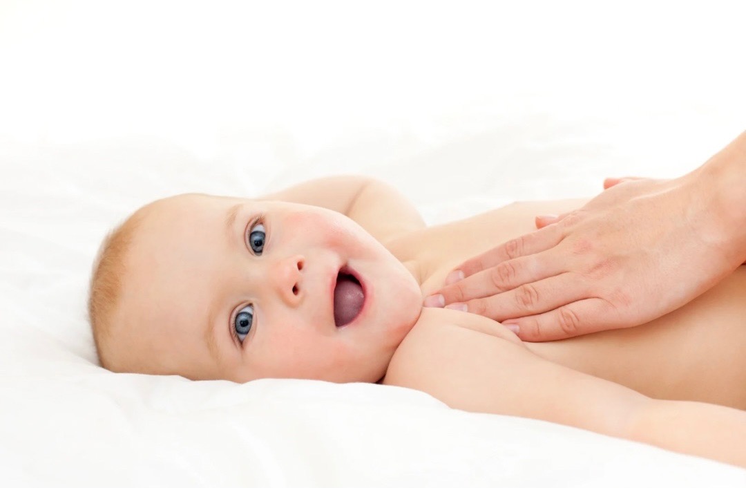 Baby laying down looking at the camera. Hands are massaging baby